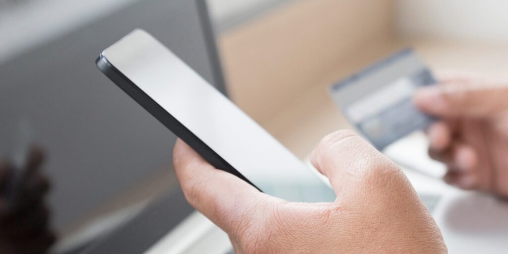 A person holding a smartphone in one hand and a credit card in the other, with a blurred background.