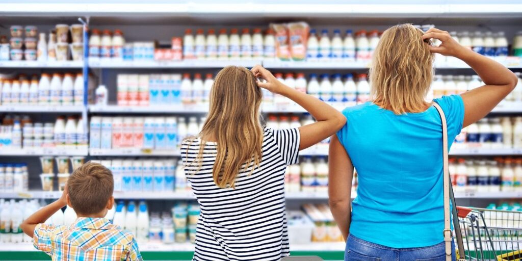 Three people in a grocery store, scratching their heads while facing a dairy aisle filled with products.