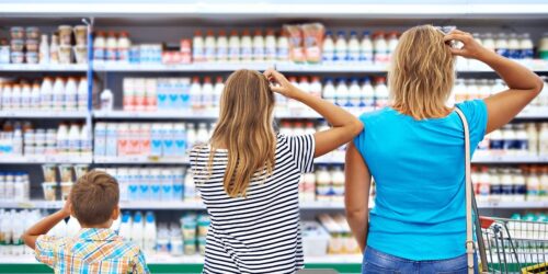 Three people in a grocery store, scratching their heads while facing a dairy aisle filled with products.