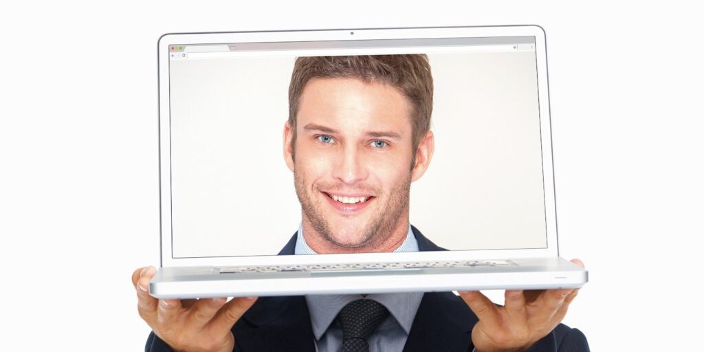 A person holding a laptop with a man's face displayed on the screen.