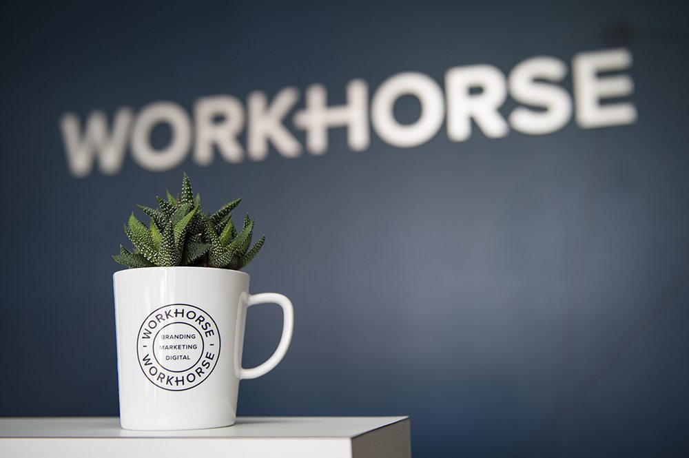 A coffee cup on a desk at the Workhorse office with the Workhorse logo on a wall in the background.