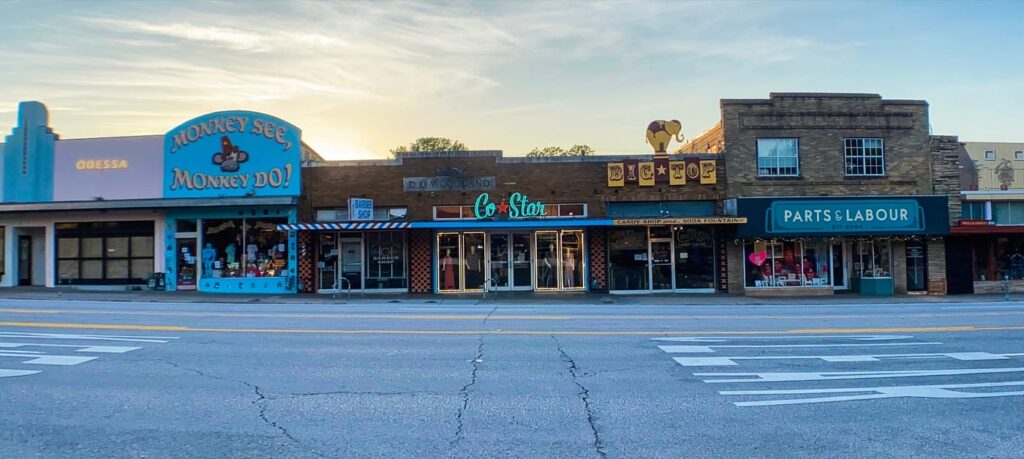 A street view of vintage-style South Congress storefronts with colorful signs at sunset.