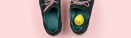 A small yellow rubber duck sitting in one of a pair of dark green shoes.