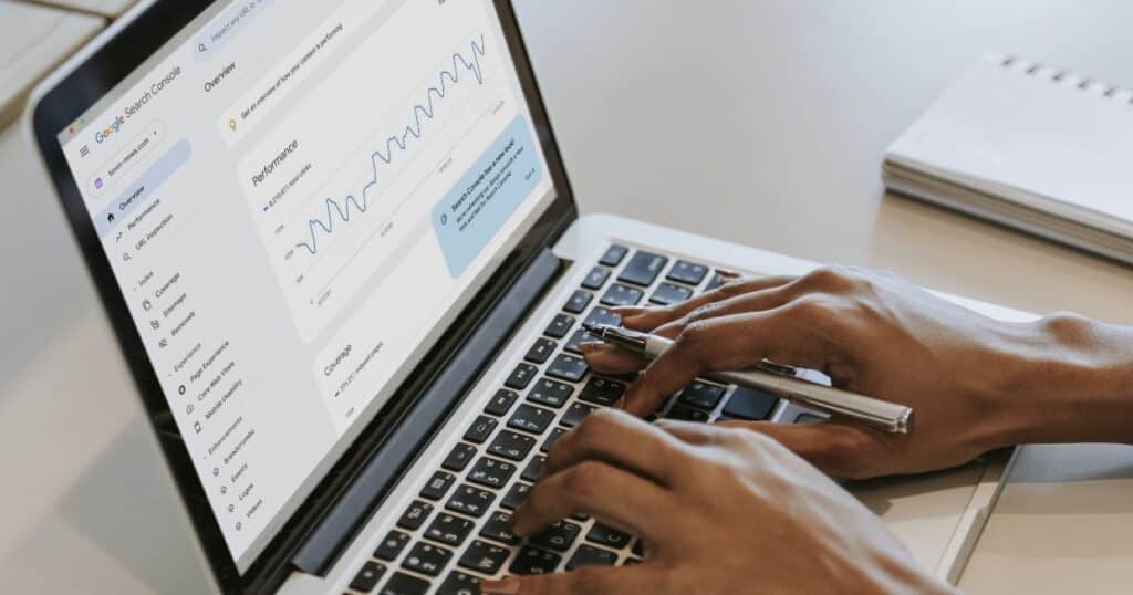A person typing on a laptop displaying Google Search Console with performance graphs on the screen.