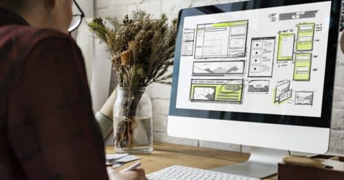 A person working on custom website UI design sketches displayed on a computer screen.