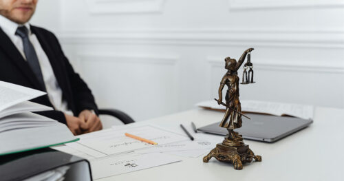 A lawyer working on their desk with files, a laptop and a statue of Lady Justice